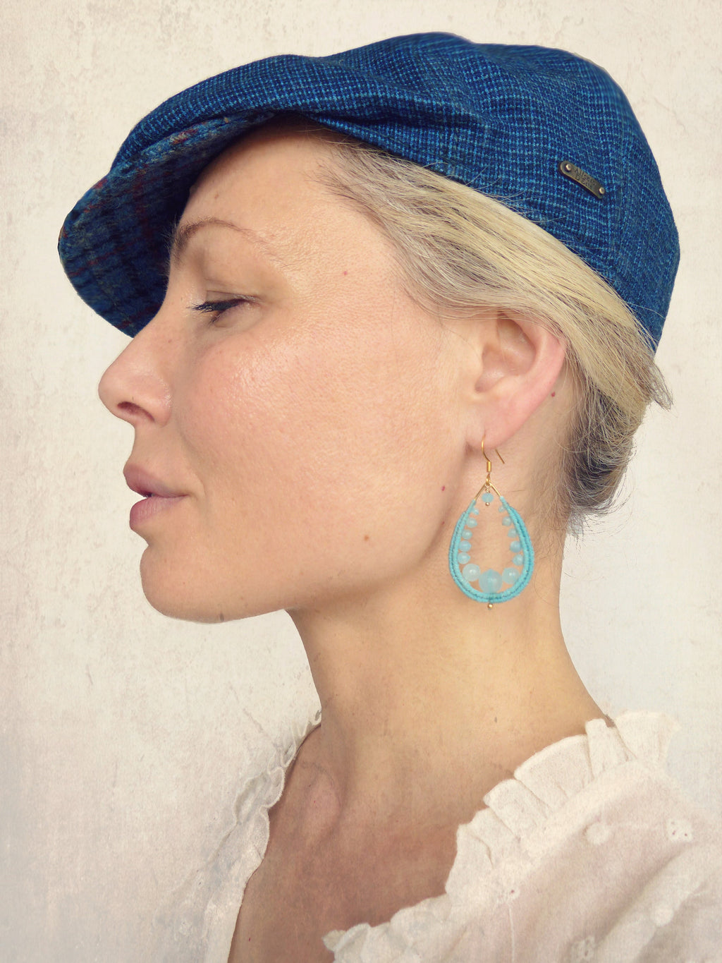Peut inclure: Une femme portant une casquette de newsboy à motif bleu et une blouse blanche avec une boucle d'oreille pendante en forme de larme turquoise.