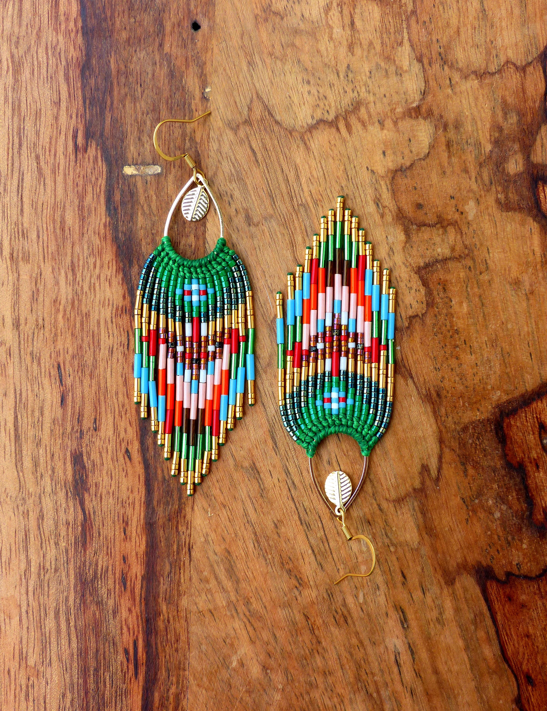 Peut inclure: Une paire de longues boucles d'oreilles en perles avec un motif de couleurs vert, rouge, bleu et or. Les boucles d'oreilles sont en forme de larme et ont un charme en forme de feuille en haut.