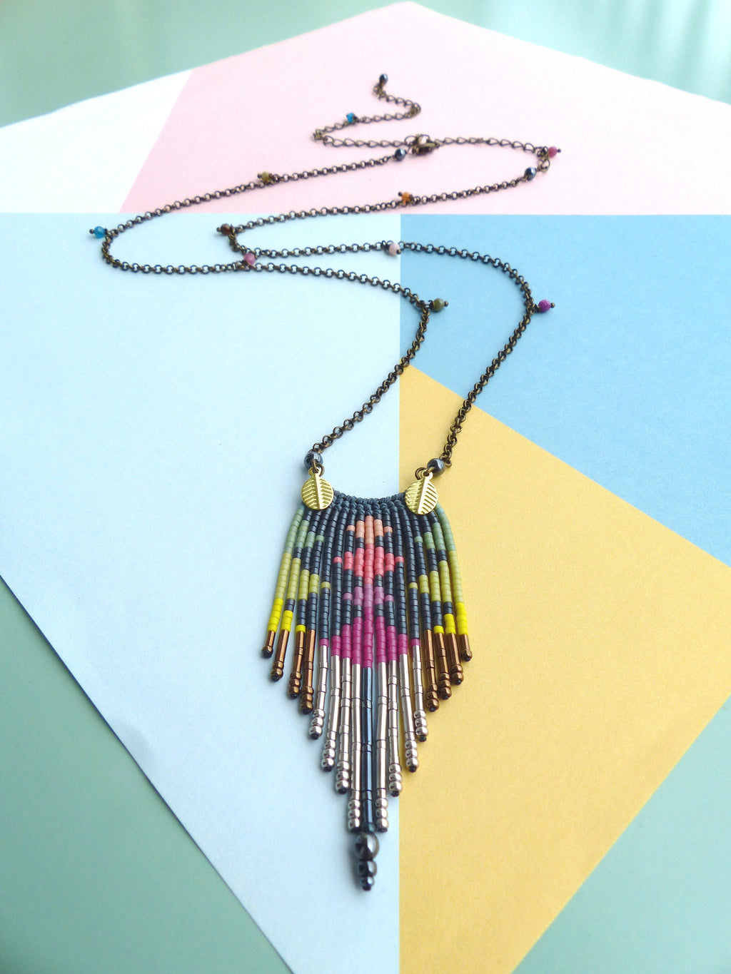 Peut inclure: Un collier de perles coloré avec un motif géométrique et un long pendentif en forme de glands. Le collier est composé de perles noires, roses, jaunes et vertes, et a une chaîne argentée et dorée.