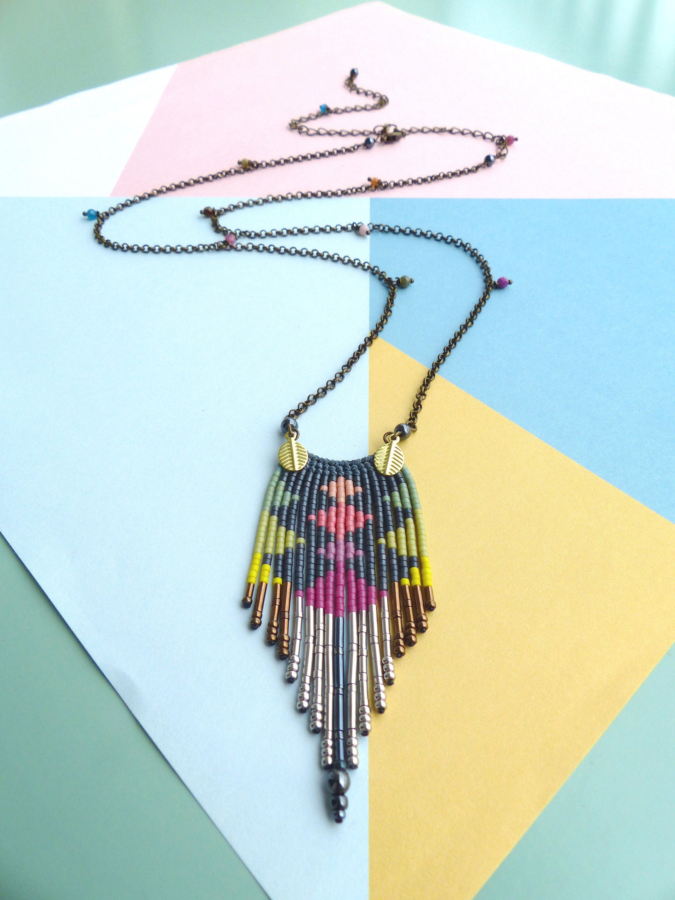 Peut inclure: Un collier de perles coloré avec un motif géométrique et un long pendentif en forme de glands. Le collier est composé de perles noires, roses, jaunes et vertes, et a une chaîne argentée et dorée.