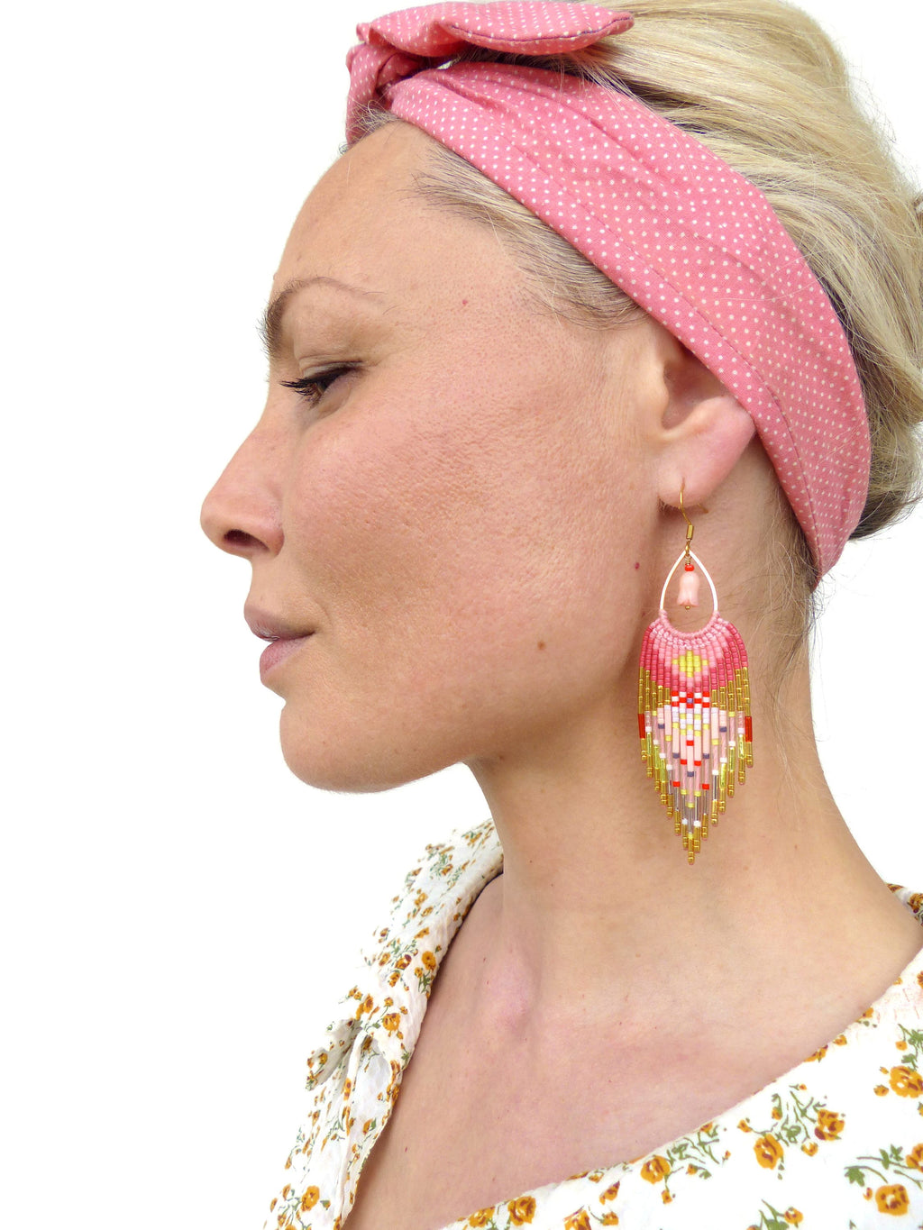Peut inclure: Une paire de boucles d'oreilles en perles roses, dorées et blanches avec un design en frange. Les boucles d'oreilles pendent des oreilles d'une personne portant un bandeau rose.
