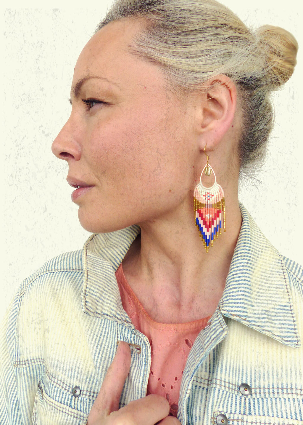 Peut inclure: Une femme portant une veste en jean rayée avec une paire de longues boucles d'oreilles en perles. Les boucles d'oreilles sont blanches, roses, bleues et dorées avec un motif géométrique.