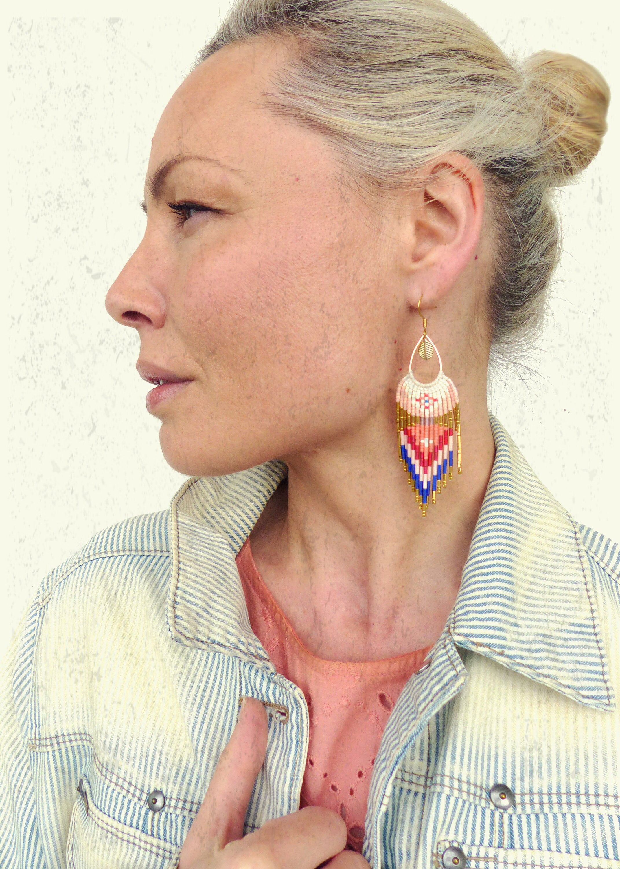 Peut inclure: Une femme portant une veste en jean rayée avec une paire de longues boucles d'oreilles en perles. Les boucles d'oreilles sont blanches, roses, bleues et dorées avec un motif géométrique.