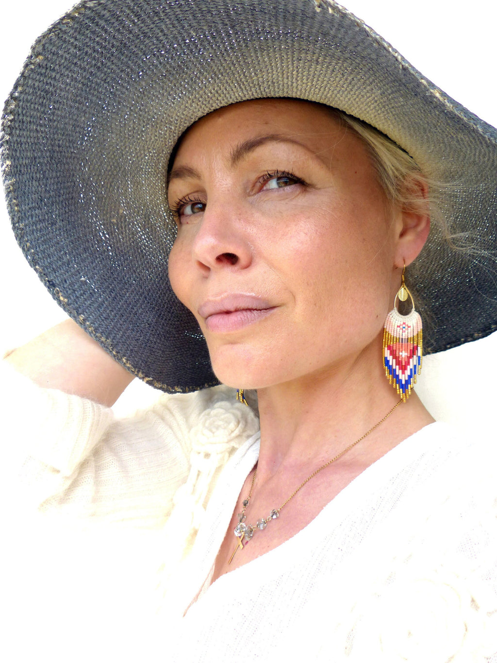 Peut inclure: Une femme portant un chapeau de paille à larges bords avec un haut blanc et un collier en or. Elle porte de longues boucles d'oreilles en perles colorées.