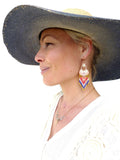 Peut inclure: Une femme portant un chapeau de paille à larges bords avec un bandeau bleu et un pull en crochet blanc. Elle porte un collier en or avec des perles de cristal claires et une paire de longues boucles d'oreilles en perles avec un motif géométrique dans les tons de rouge, bleu et blanc.