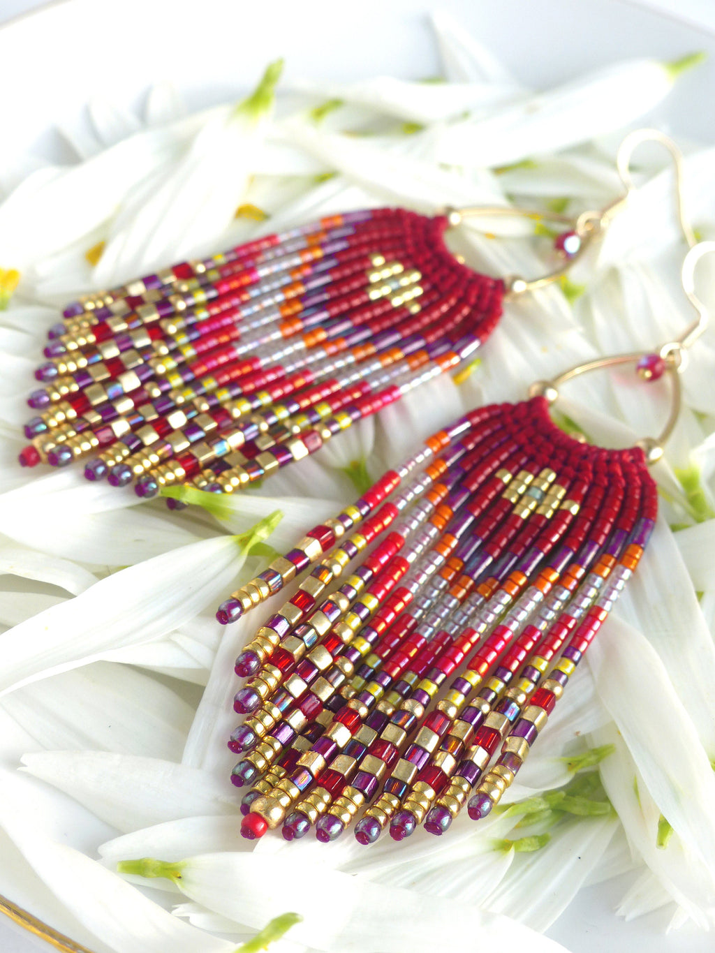 Peut inclure: Une paire de longues boucles d'oreilles en perles avec un motif rouge, or et violet. Les boucles d'oreilles sont faites de petites perles carrées et ont un design en forme de frange.