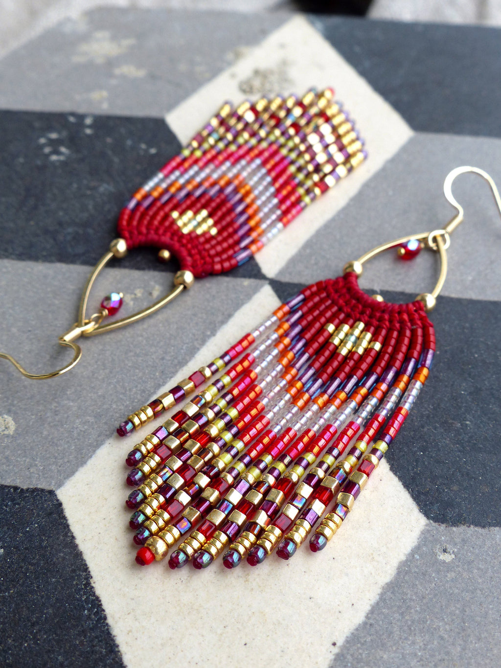 Peut inclure: Boucles d'oreilles en perles rouges, dorées et blanches avec un design en frange. Les boucles d'oreilles sont faites de petites perles colorées et ont un fermoir crochet doré.