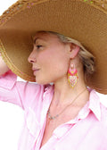 Peut inclure: Une femme portant une chemise rose et un chapeau de paille à larges bords avec des boucles d'oreilles en perles roses et dorées. 