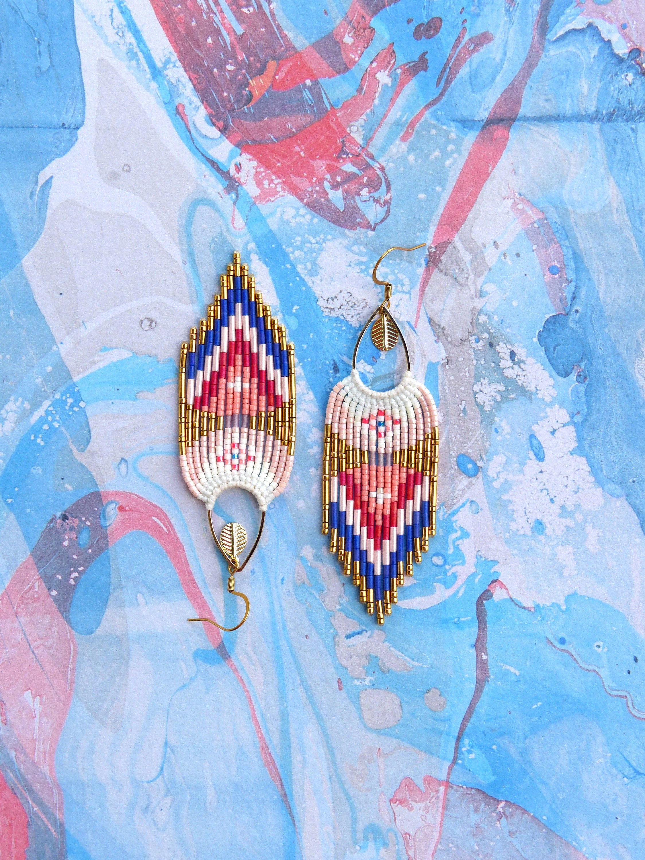 Peut inclure: Une paire de longues boucles d'oreilles en perles avec un motif géométrique. Les boucles d'oreilles sont faites de perles blanches, roses, bleues et dorées. Les boucles d'oreilles ont une forme de larme et sont suspendues à des crochets dorés.