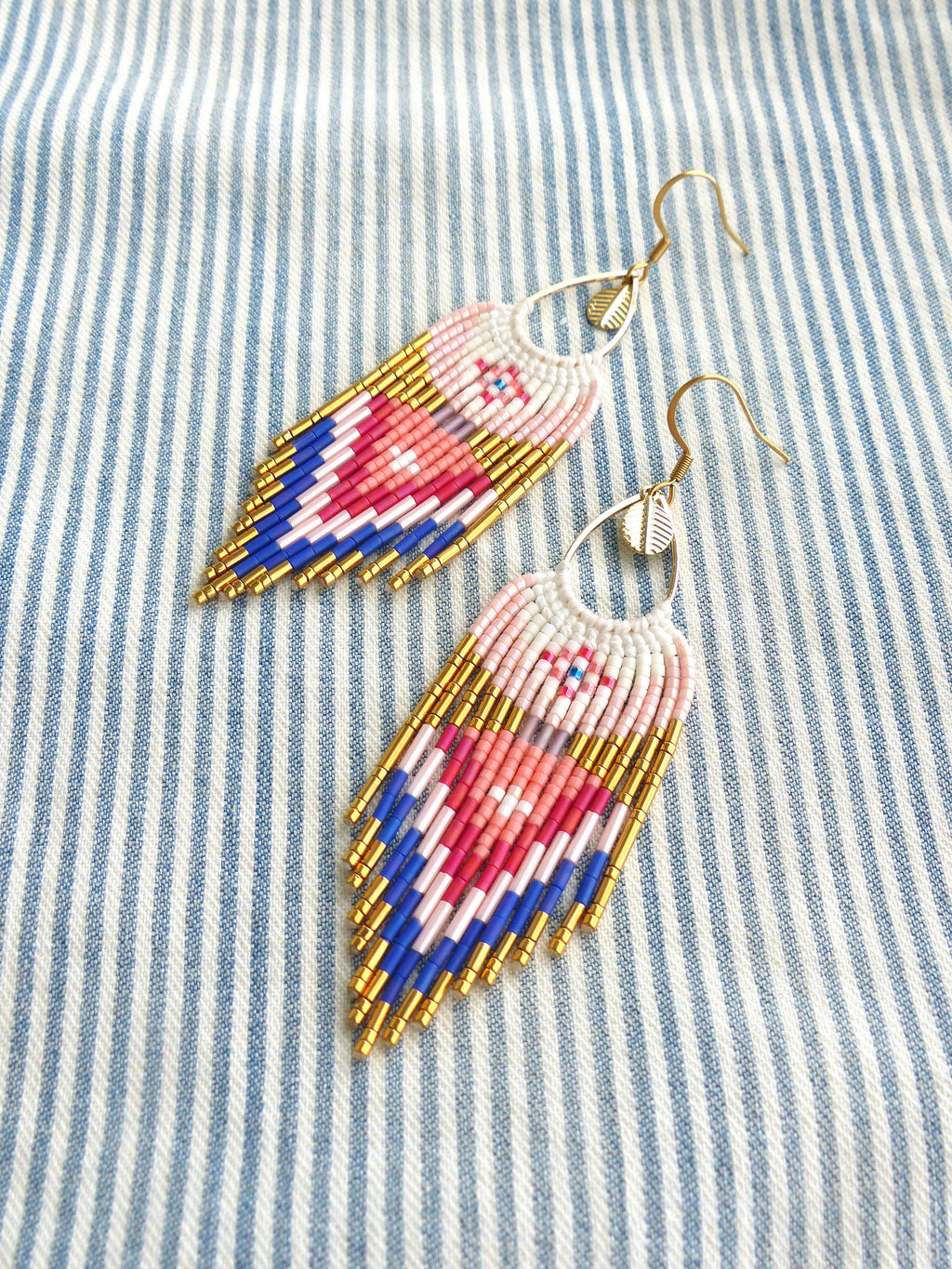 Peut inclure: Une paire de longues boucles d'oreilles en forme de larme. Les boucles d'oreilles sont faites de perles blanches, roses, bleues et dorées. Les boucles d'oreilles ont une fermeture à crochet dorée.