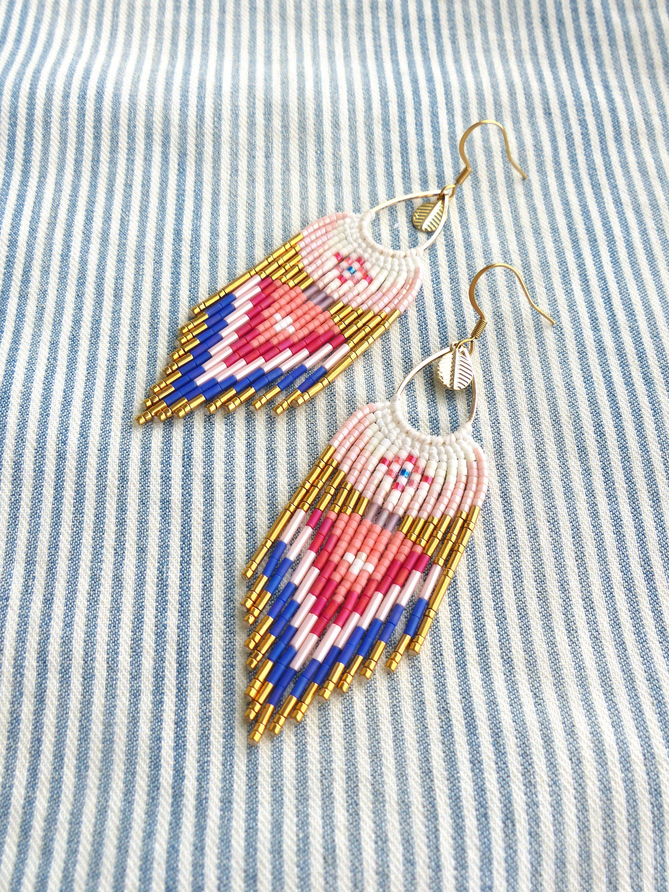 Peut inclure: Une paire de longues boucles d'oreilles en forme de larme. Les boucles d'oreilles sont faites de perles blanches, roses, bleues et dorées. Les boucles d'oreilles ont une fermeture à crochet dorée.