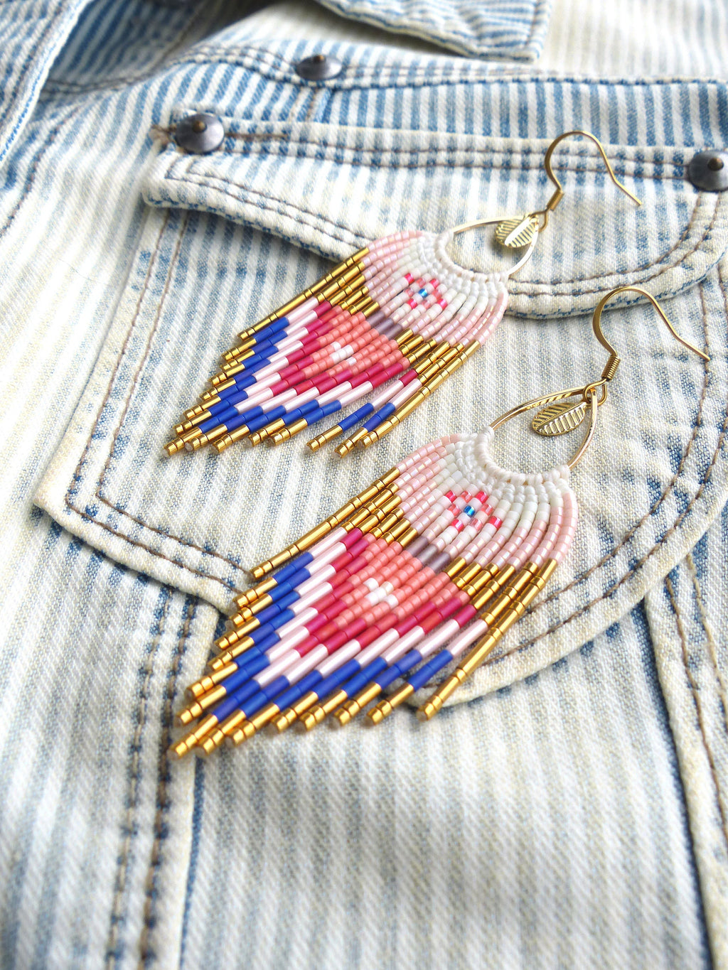 Peut inclure: Une paire de boucles d'oreilles pendantes avec un motif géométrique de perles roses, bleues et blanches. Les boucles d'oreilles sont en métal doré et ont un charme en forme de feuille.