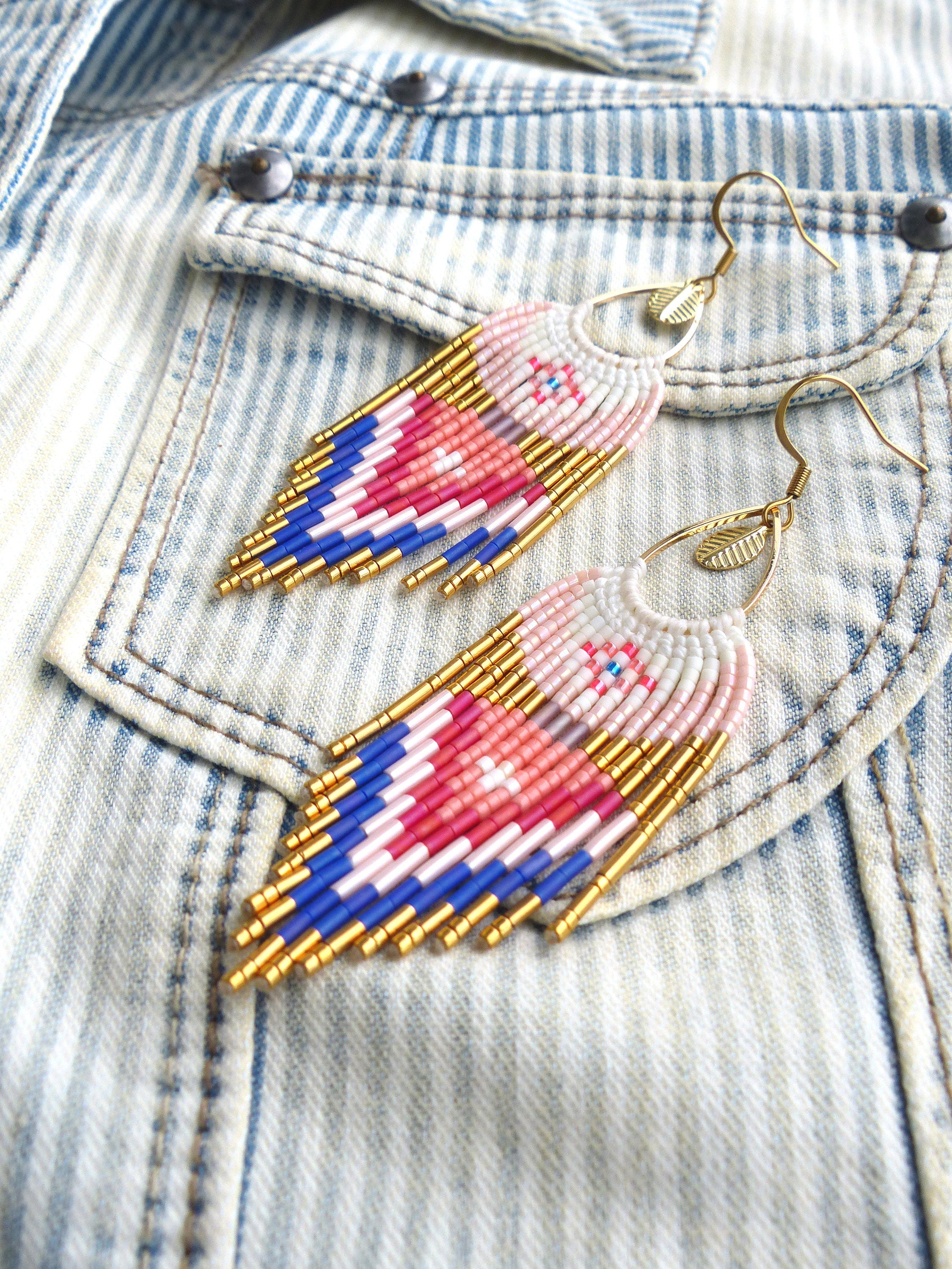 Peut inclure: Une paire de boucles d'oreilles pendantes avec un motif géométrique de perles roses, bleues et blanches. Les boucles d'oreilles sont en métal doré et ont un charme en forme de feuille.