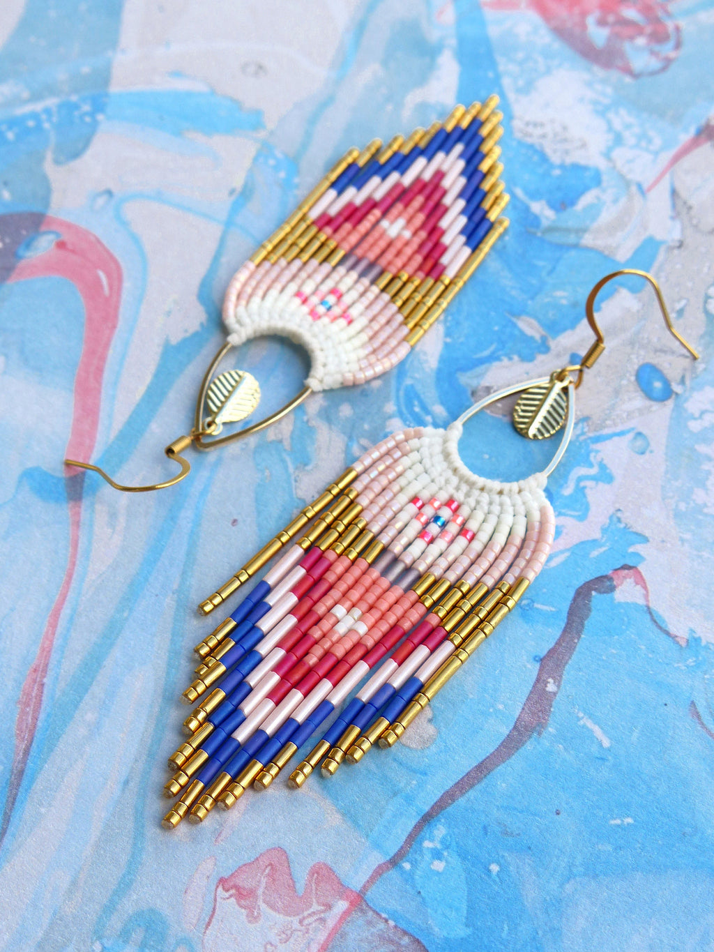 Peut inclure: Une paire de longues boucles d'oreilles en perles avec un motif géométrique dans des tons de rose, bleu et or. Les boucles d'oreilles sont faites de petites perles de rocaille et ont un design en forme de frange.