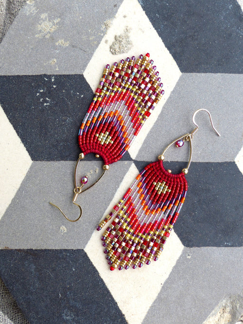 Peut inclure: Une paire de longues boucles d'oreilles en perles avec un motif rouge, orange et or. Les boucles d'oreilles sont faites de petites perles colorées et ont un design en forme de frange.