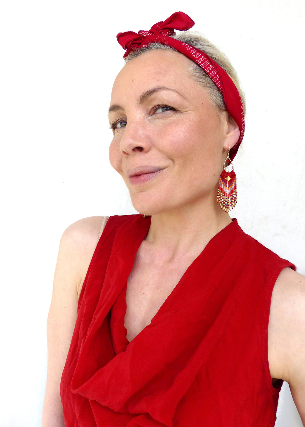 Peut inclure: Une femme portant un haut rouge sans manches avec un bandana rouge noué autour de la tête. Elle porte de longues boucles d'oreilles en perles avec des accents rouges, dorés et blancs.