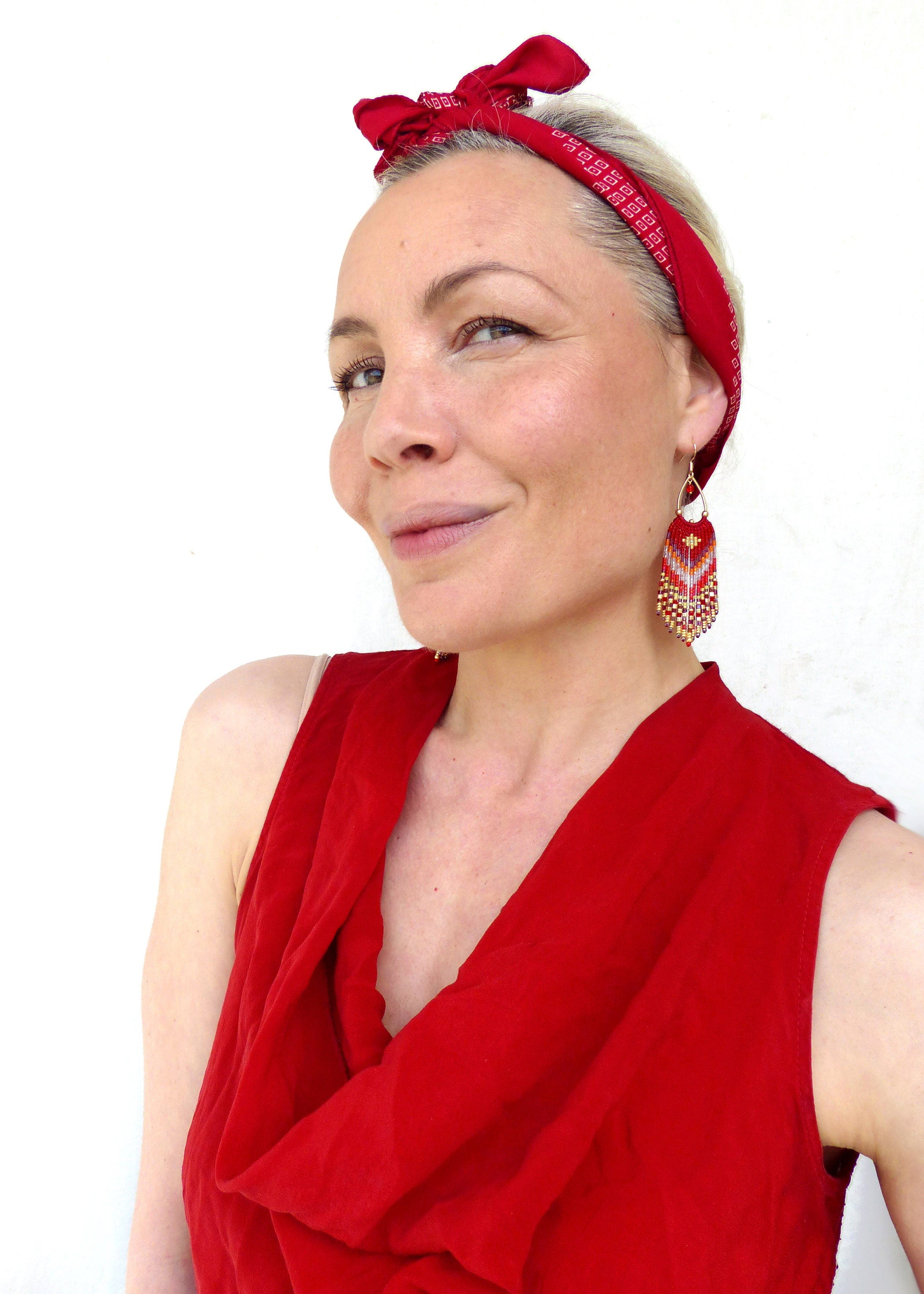 Peut inclure: Une femme portant un haut rouge sans manches avec un bandana rouge noué autour de la tête. Elle porte de longues boucles d'oreilles en perles avec des accents rouges, dorés et blancs.