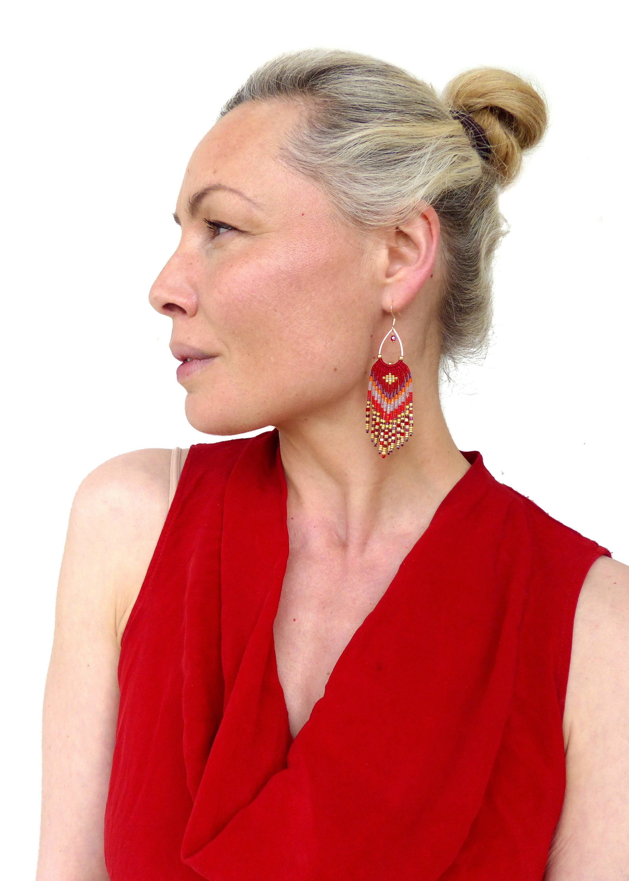 Peut inclure: Une femme portant un haut rouge sans manches avec une paire de longues boucles d'oreilles en perles rouges, orange et dorées.