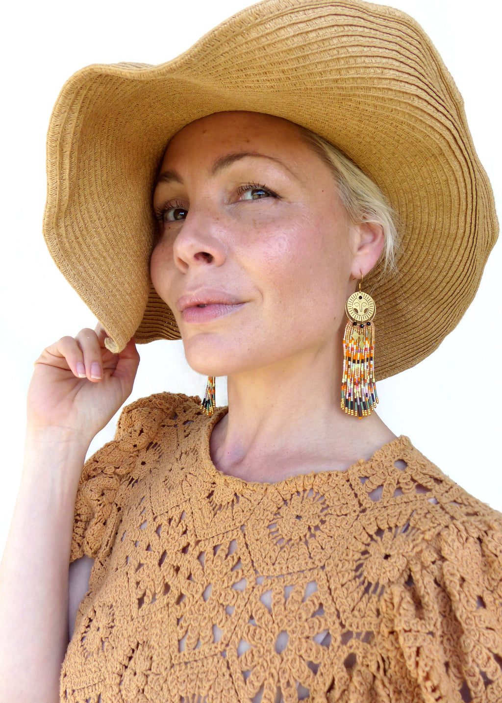 Peut inclure: Une femme portant un chapeau de paille et un haut en crochet avec de longues boucles d'oreilles en perles ornées d'un pendentif soleil en or.