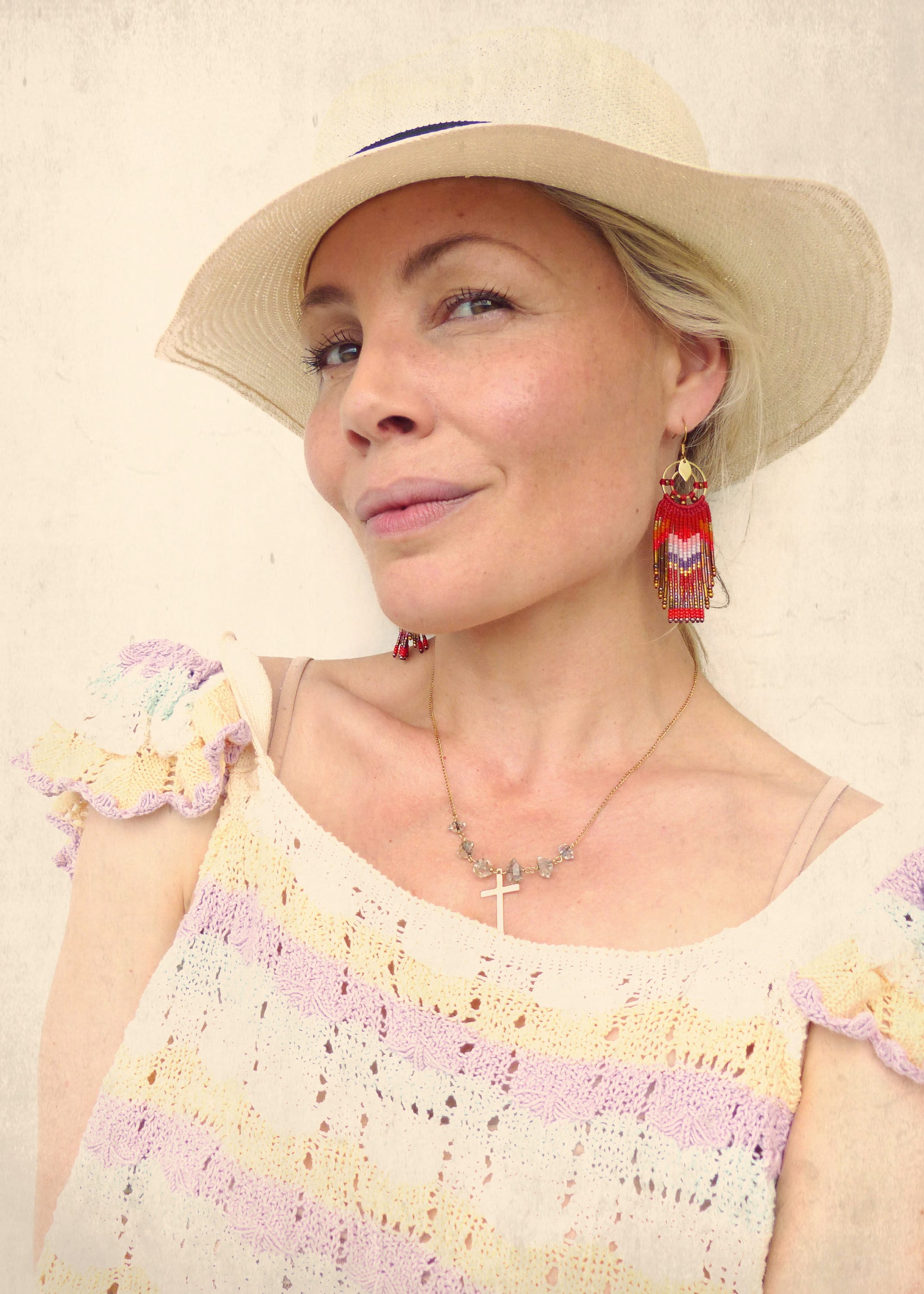 Peut inclure: Une femme portant un haut en crochet blanc avec un motif rayé rose clair et jaune. Elle porte un chapeau de paille et un collier en or avec un pendentif en forme de croix. Elle porte également de longues boucles d'oreilles en perles rouges.