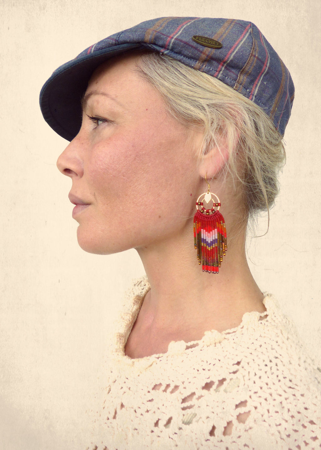 Peut inclure: Une femme portant une casquette de newsboy bleu et blanc à carreaux avec des boucles d'oreilles en perles rouges et blanches. Les boucles d'oreilles sont longues et pendantes, avec un motif géométrique.