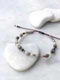 Peut inclure: Un bracelet délicat composé de perles grises, noires, blanches et roses. Le bracelet est fait de pierres naturelles et présente une fermeture simple à nœud.