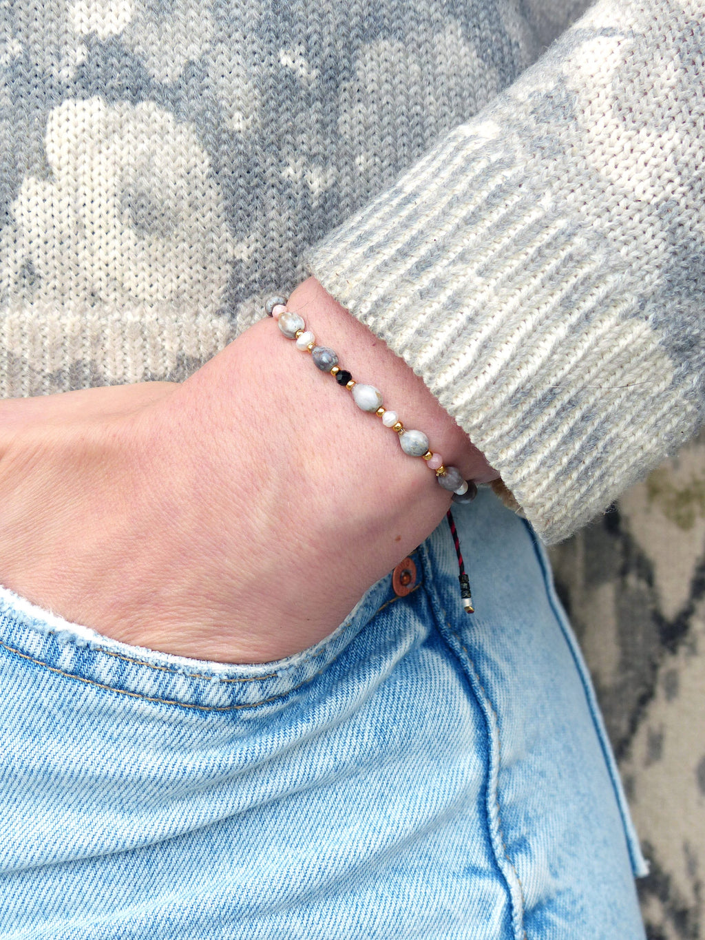 Peut inclure: Un bracelet avec des perles blanches, grises et noires sur une chaîne dorée. Le bracelet est attaché avec un cordon rouge et noir.