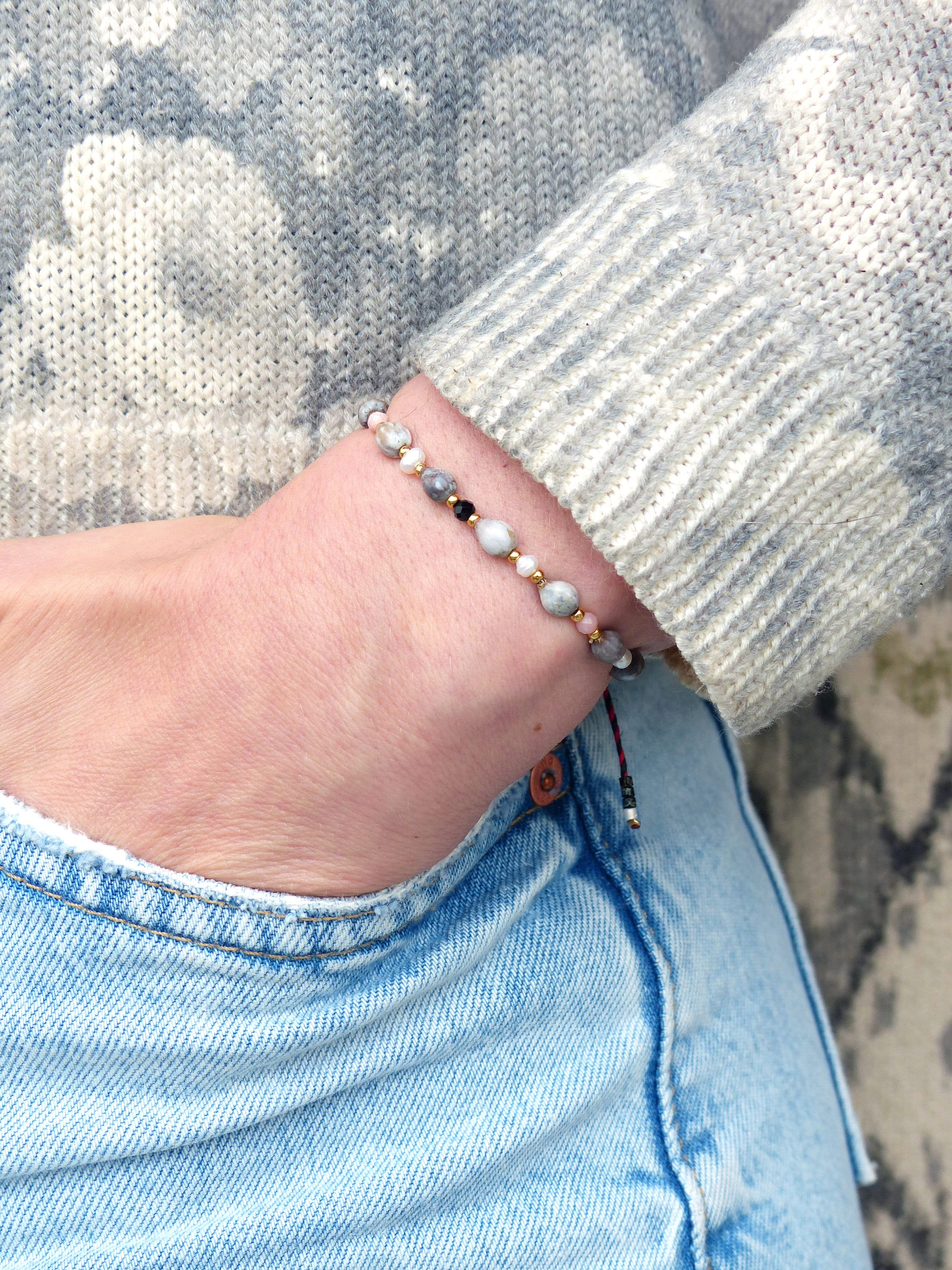 Peut inclure: Un bracelet avec des perles blanches, grises et noires sur une chaîne dorée. Le bracelet est attaché avec un cordon rouge et noir.