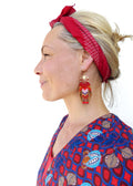 Peut inclure: Une femme portant un bandana rouge et une boucle d'oreille en franges de perles rouges, bleues et dorées. La boucle d'oreille a un cercle doré avec un motif en forme de cœur.