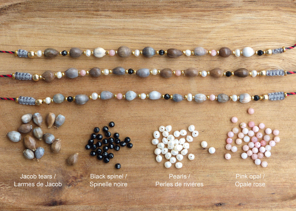 Peut inclure: Trois rangs de bijoux avec différentes perles, dont des perles brunes, grises, roses, blanches et noires. Les perles sont disposées en rangée sur une surface en bois. En dessous des bijoux se trouvent des tas de perles en vrac des mêmes couleurs. Le texte sous les perles indique "Jacob tears / Larmes de Jacob", "Black spinel / Spinelle noire", "Pearls / Perles de rivières", et "Pink opal / Opale rose".