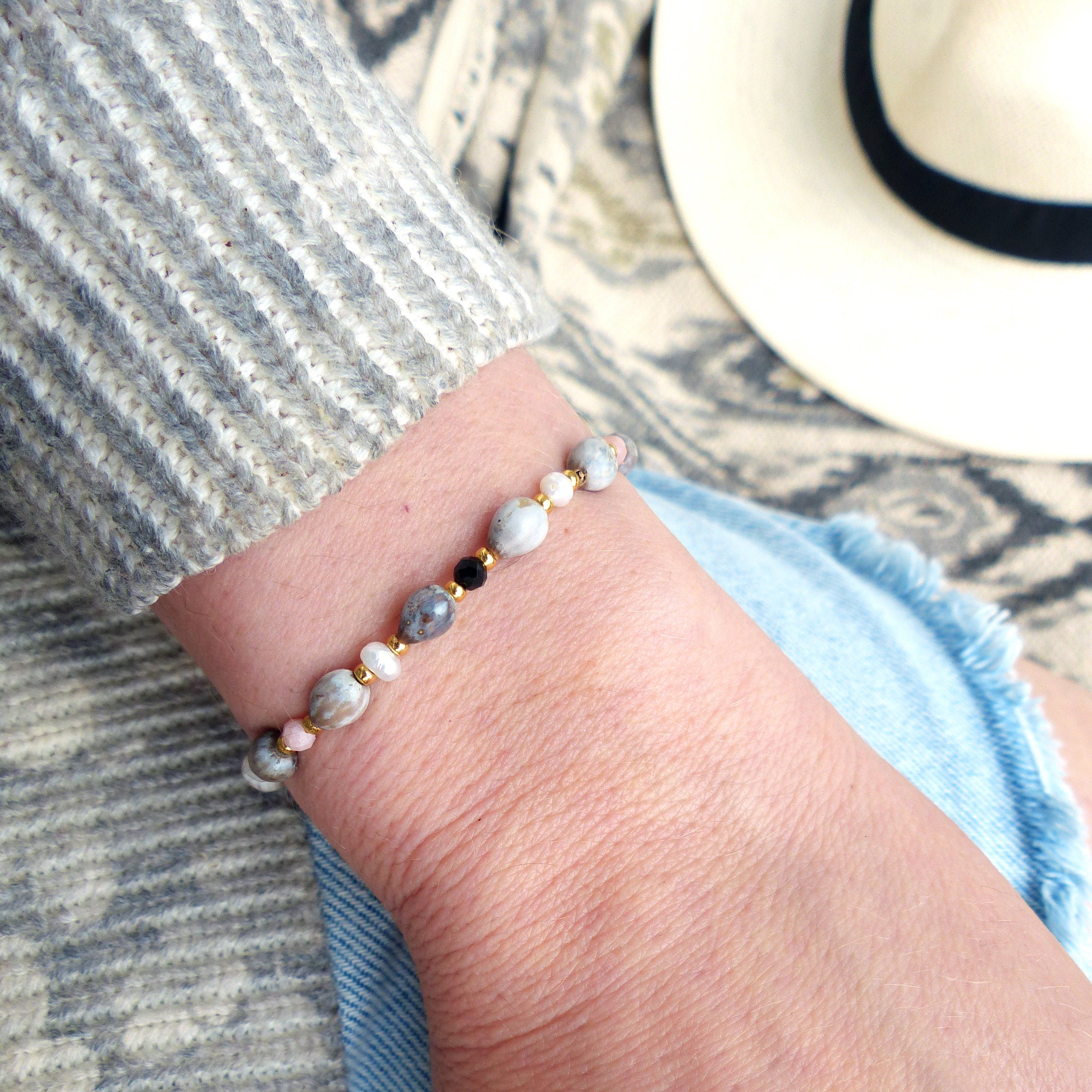 Peut inclure: Un bracelet avec des perles grises, roses et noires sur une chaîne dorée.