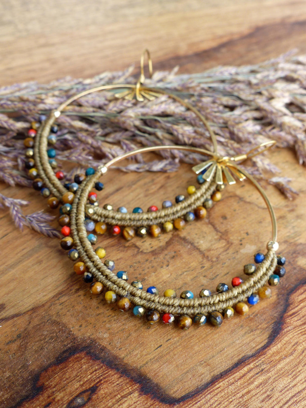 Peut inclure: Boucles d'oreilles créoles dorées avec des perles brunes, dorées et multicolores. Les perles sont disposées en cercle autour du cerceau.