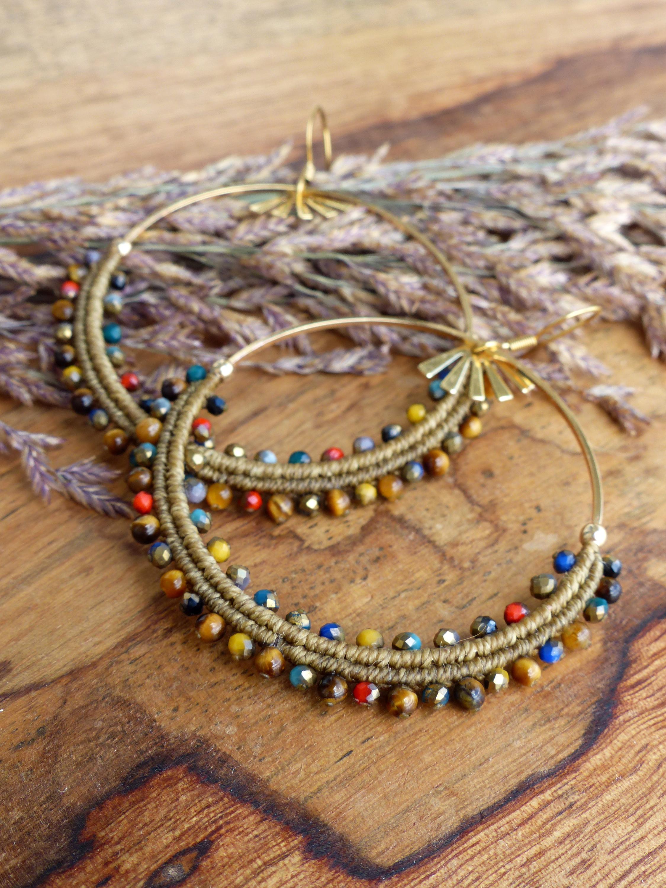 Peut inclure: Boucles d'oreilles créoles dorées avec des perles brunes, dorées et multicolores. Les perles sont disposées en cercle autour du cerceau.