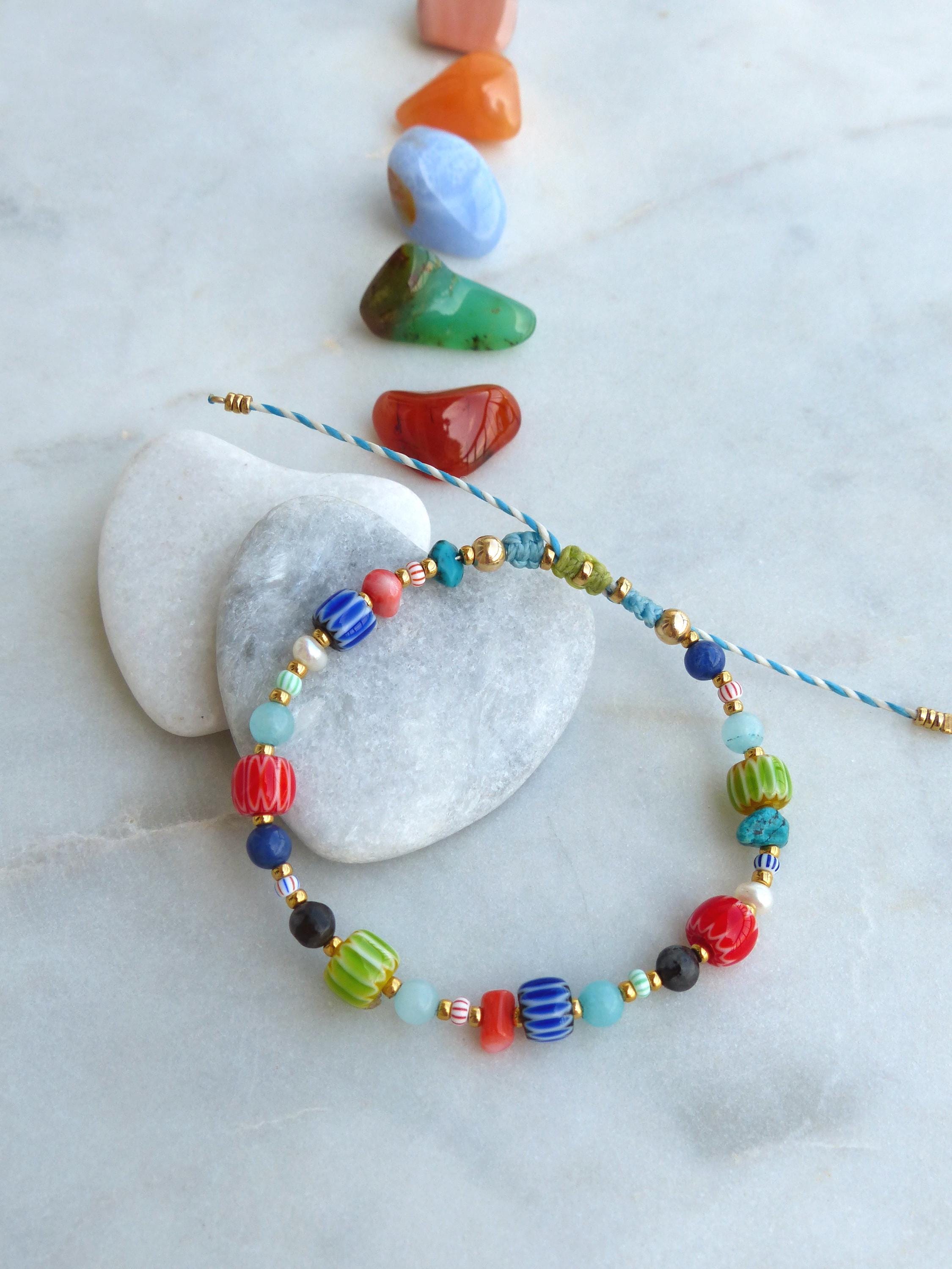 Peut inclure: Un bracelet coloré composé de perles de verre de différentes couleurs, notamment bleu, vert, rouge et blanc. Le bracelet est noué avec un cordon bleu et blanc et possède un fermoir doré.