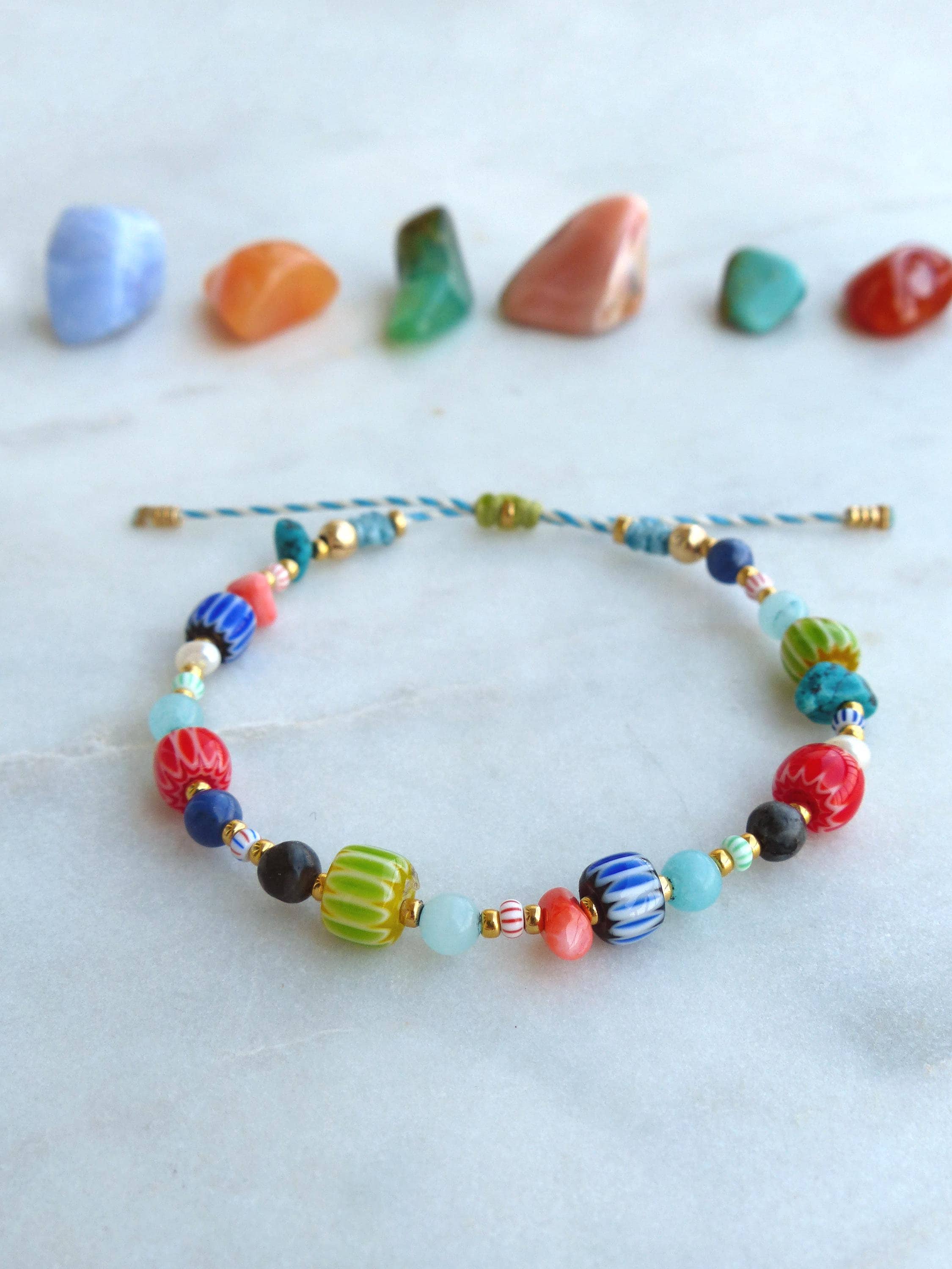 Peut inclure: Un bracelet coloré en perles avec une variété de perles en verre, notamment bleues, vertes, rouges et blanches. Le bracelet est noué avec un cordon bleu et blanc et présente des accents dorés.