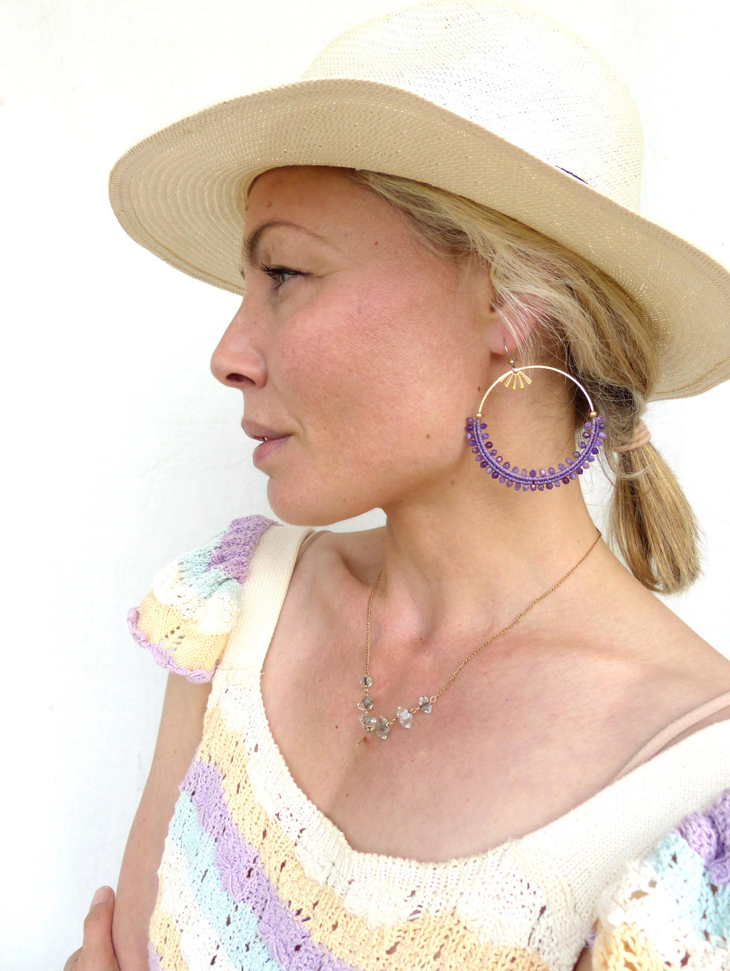 Peut inclure: Un chapeau de soleil couleur paille à larges bords. Boucles d'oreilles créoles dorées avec des perles violettes et un collier pendentif doré avec des pierres transparentes. Le haut est à motifs arc-en-ciel pastel.