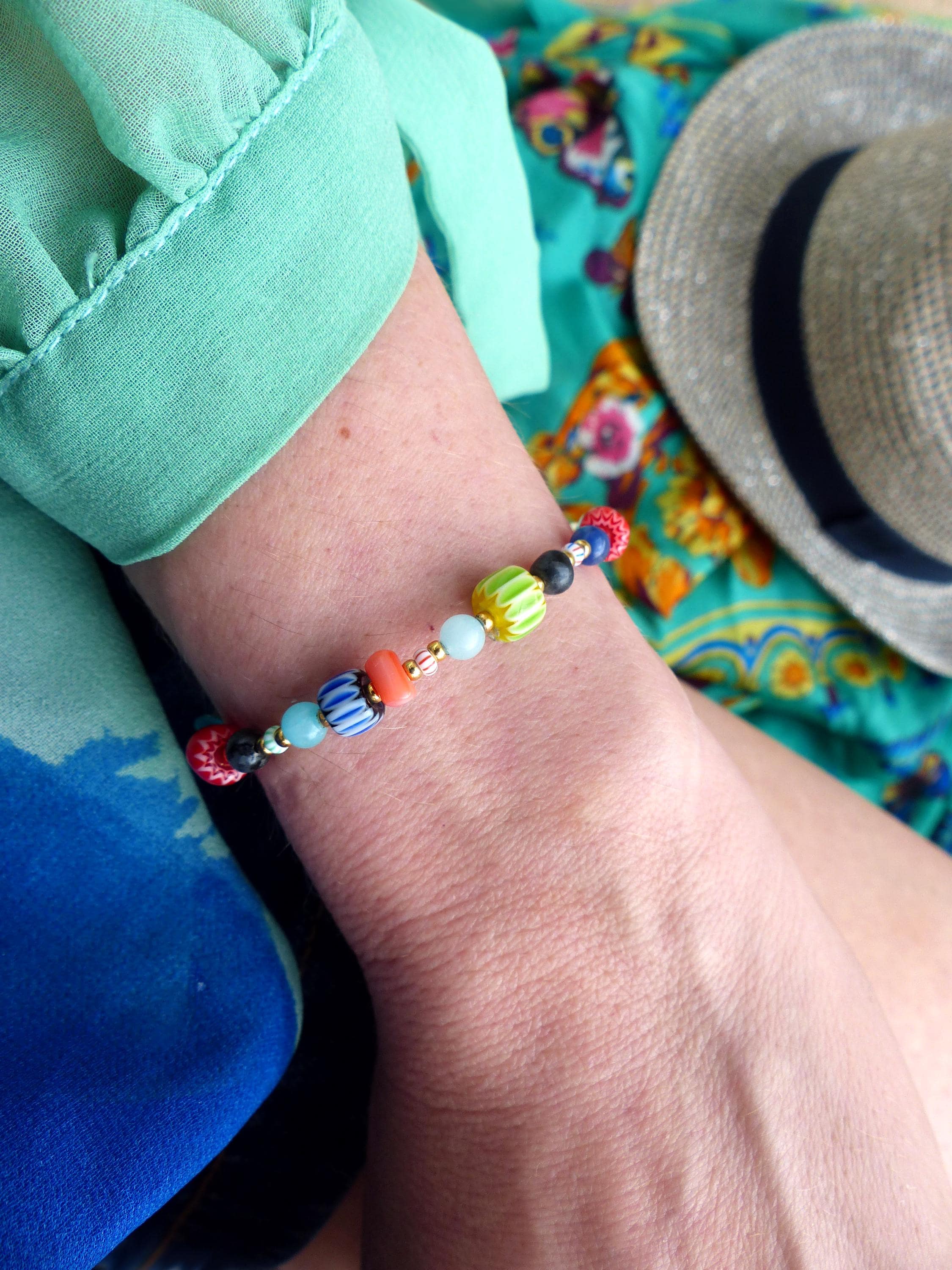 Peut inclure: Un bracelet coloré en perles avec des perles noires, rouges, orange, jaunes, vertes, bleues et blanches. Le bracelet est au poignet d'une personne.