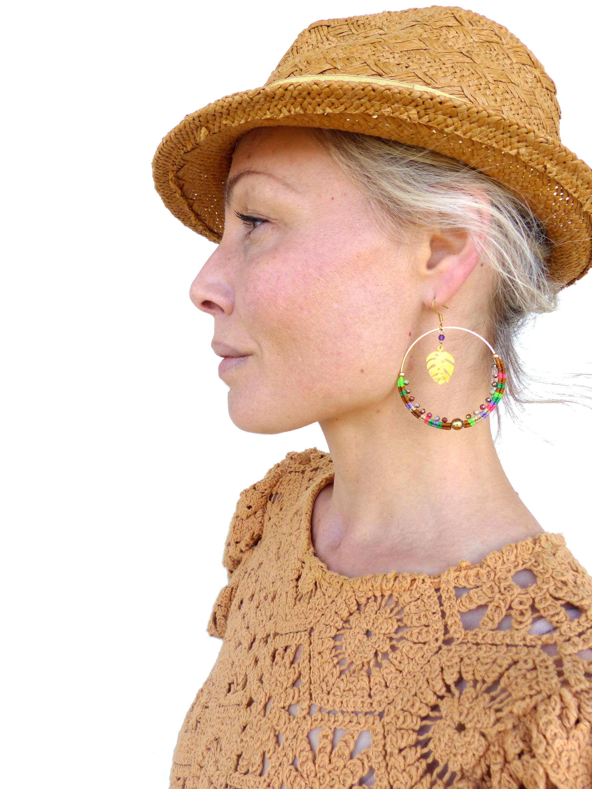 Peut inclure: Une femme portant un chapeau de paille et un haut en crochet avec des boucles d'oreilles créoles en perles colorées ornées d'un pendentif en feuille d'or.