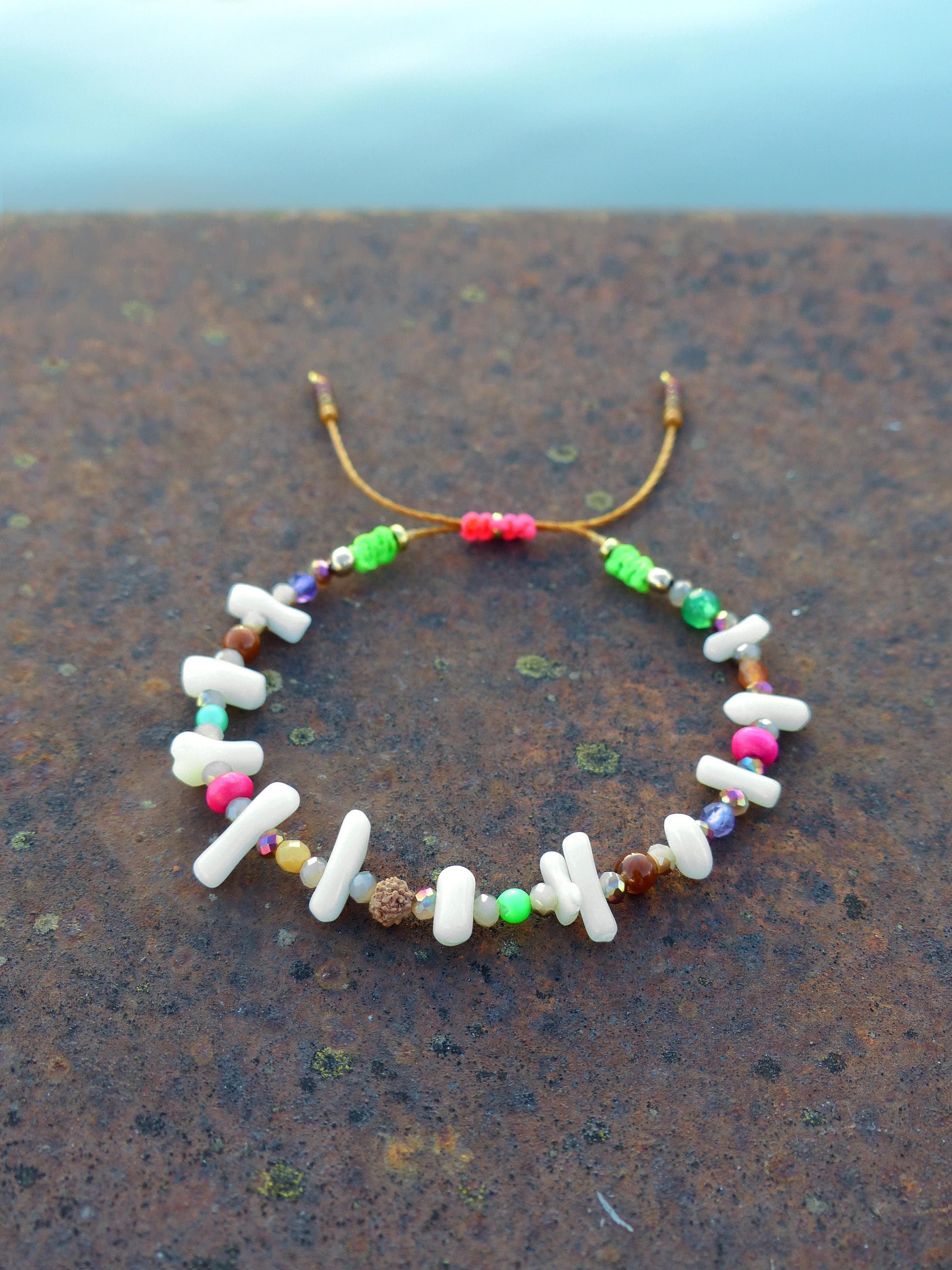 Peut inclure: Un bracelet coloré en perles avec des perles blanches, roses, vertes et brunes. Le bracelet est fait avec un cordon brun et a une fermeture à nœud.