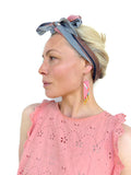 Peut inclure: Boucles d'oreilles géométriques roses et dorées avec des crochets dorés. Les boucles d'oreilles sont portées avec un haut rose et un foulard à motifs. Les boucles d'oreilles ont une forme triangulaire.