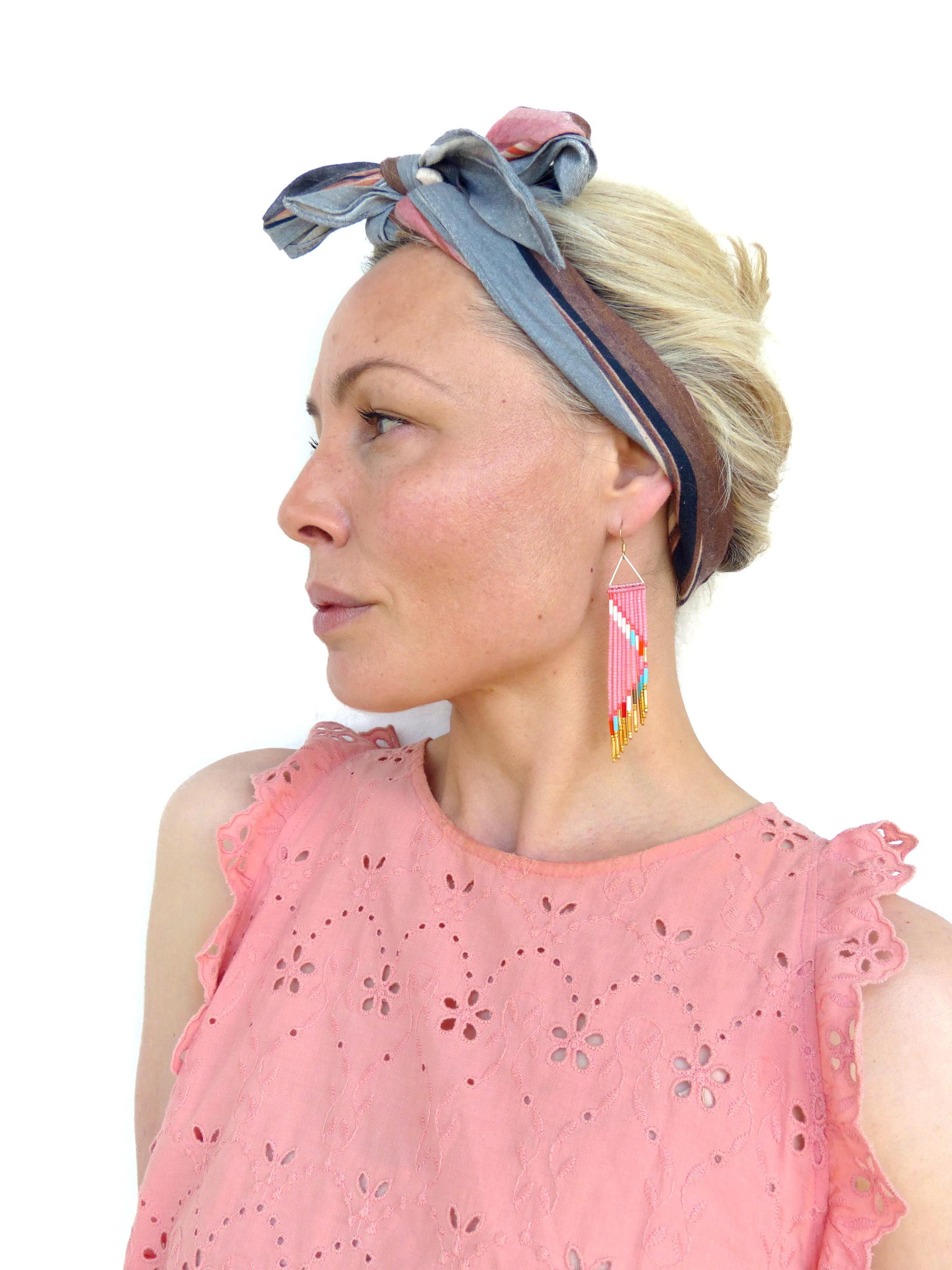 Peut inclure: Boucles d'oreilles géométriques roses et dorées avec des crochets dorés. Les boucles d'oreilles sont portées avec un haut rose et un foulard à motifs. Les boucles d'oreilles ont une forme triangulaire.
