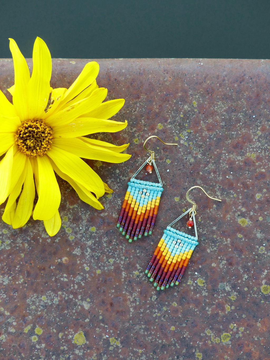 Peut inclure: Une paire de boucles d'oreilles en perles avec un schéma de couleurs turquoise, jaune, orange et rouge. Les boucles d'oreilles sont faites de petites perles et ont une forme triangulaire en haut.