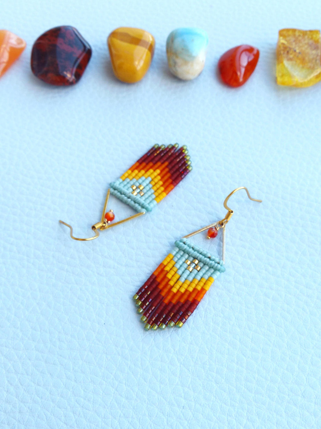 Peut inclure: Une paire de boucles d'oreilles en perles avec un motif géométrique. Les boucles d'oreilles sont faites de perles rouges, orange, jaunes et bleues. Les boucles d'oreilles sont suspendues à des crochets dorés.