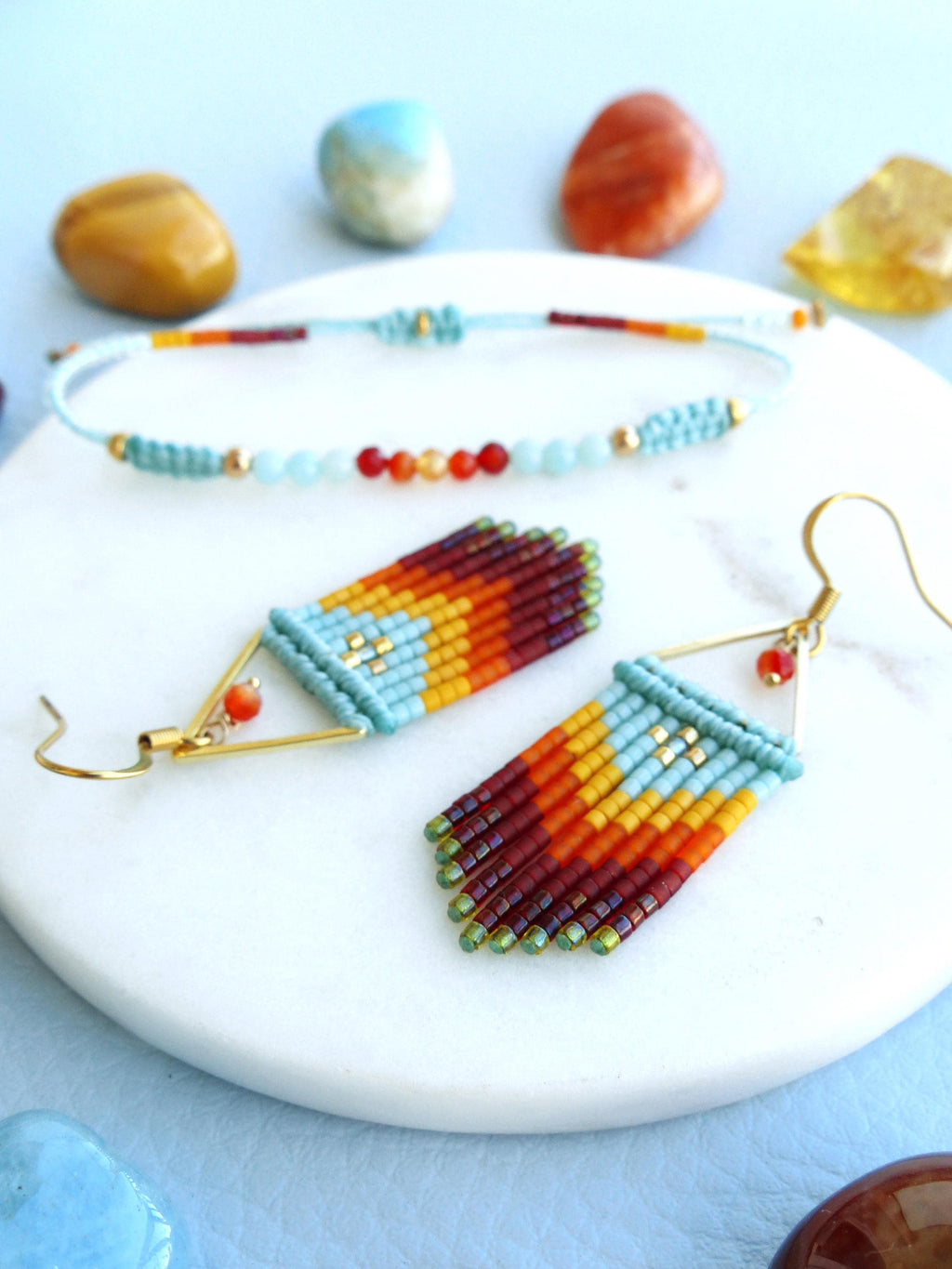 Peut inclure: Un ensemble de boucles d'oreilles et d'un bracelet assorti en perles turquoise, orange, jaune et rouge. Les boucles d'oreilles sont longues et pendantes, avec un sommet triangulaire et une frange de perles. Le bracelet est une simple bande avec une fermeture nouée.