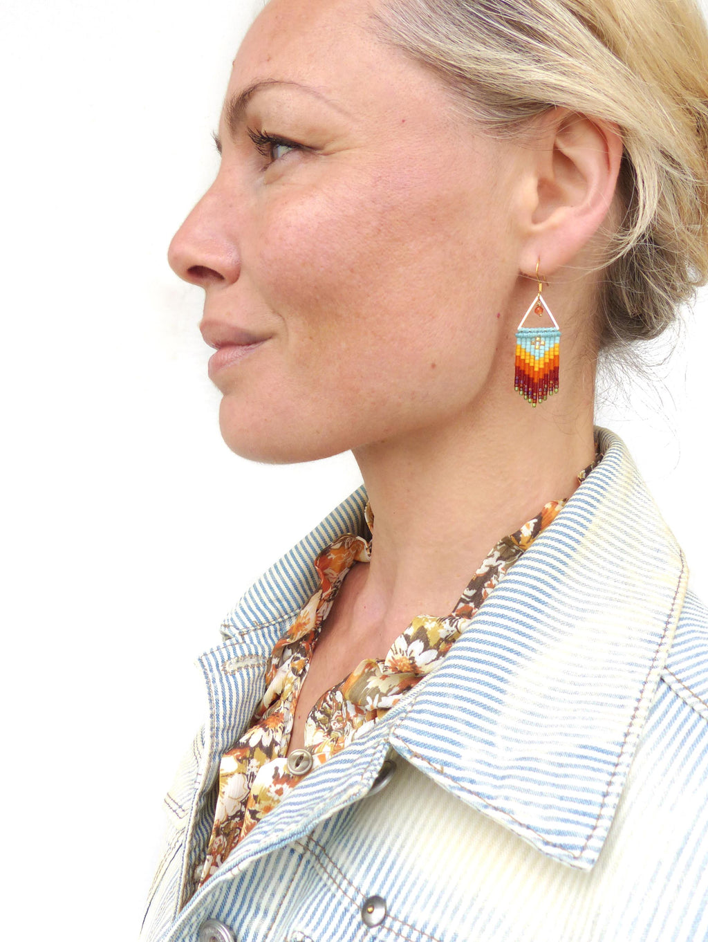 Peut inclure: Une paire de boucles d'oreilles pendantes dorées avec un motif géométrique. Les boucles d'oreilles sont faites de petites perles dans des tons de bleu, orange, rouge et marron. Les perles sont disposées en forme de chevron.