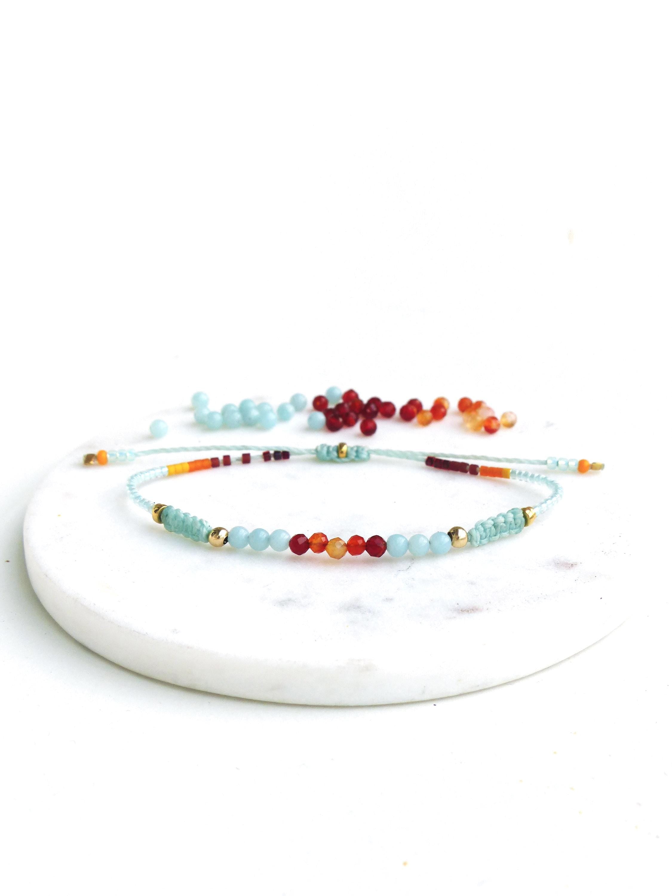 Peut inclure: Un bracelet délicat composé de perles de couleur bleu clair, orange, rouge et or. Le bracelet est réalisé avec de petites perles rondes et est attaché avec une fine ficelle.