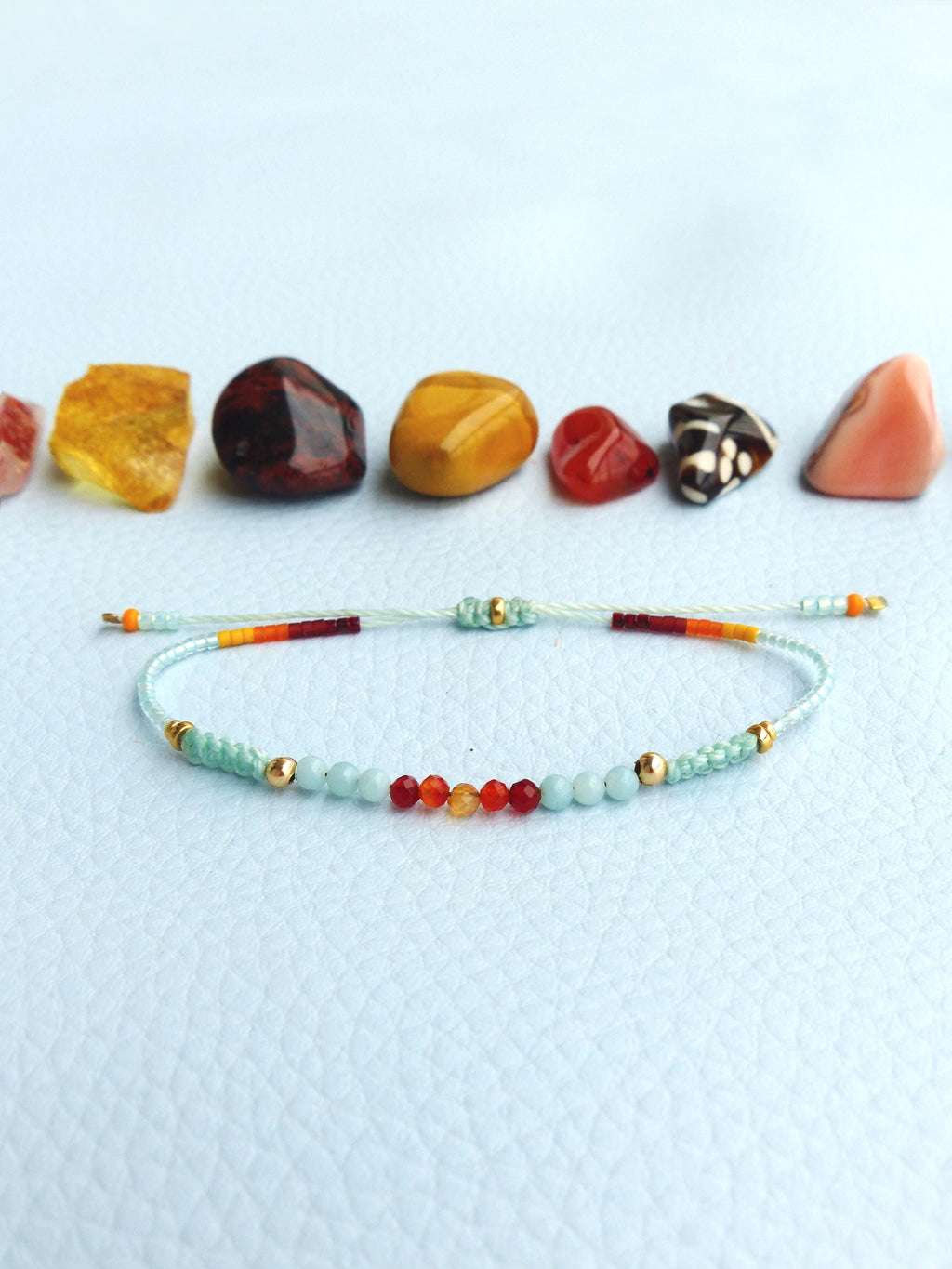 Peut inclure: Un bracelet délicat avec un arc-en-ciel de petites perles, y compris rouge, orange, jaune et bleu. Le bracelet est fait avec une fine ficelle transparente et a des accents dorés.