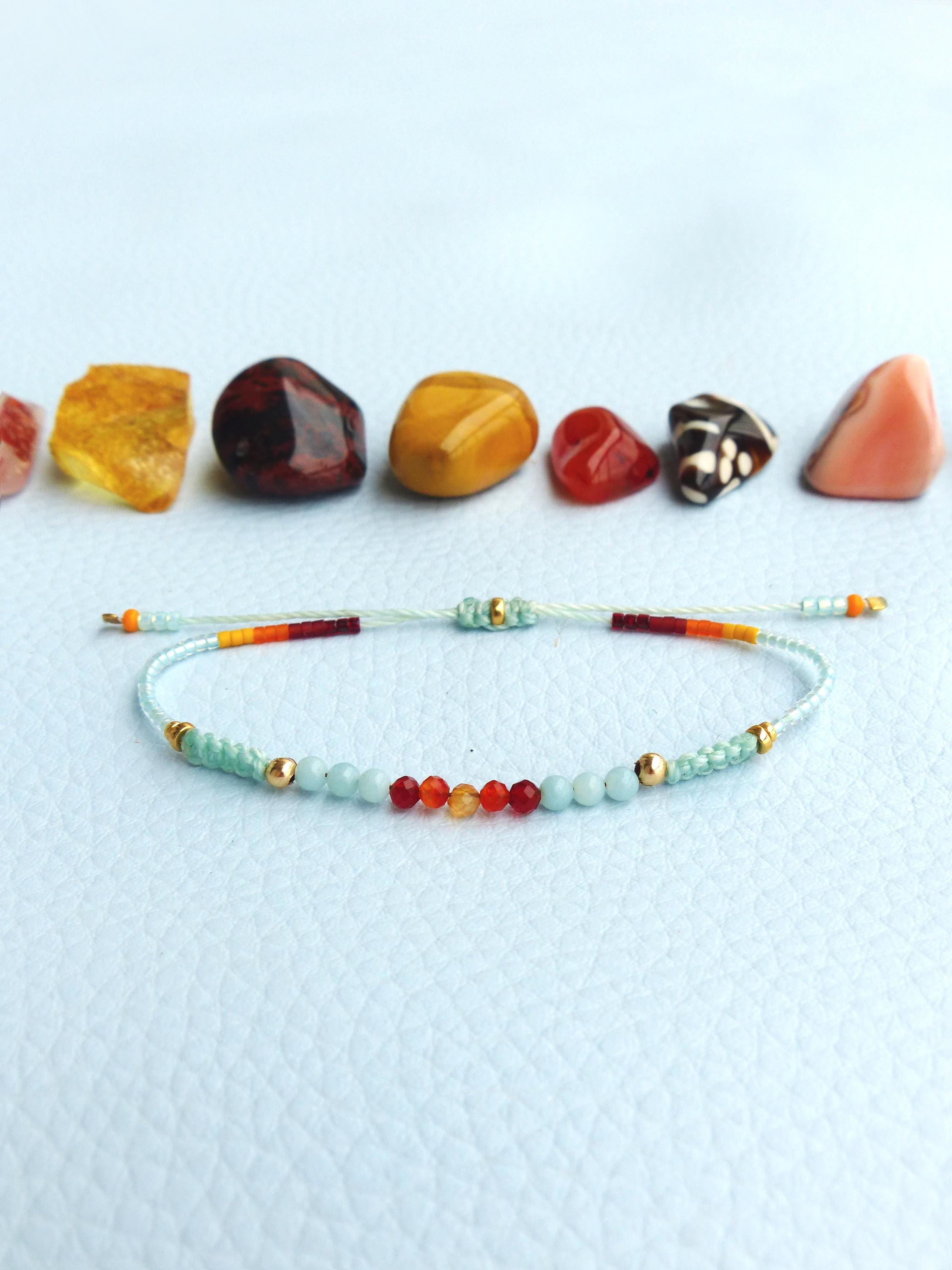 Peut inclure: Un bracelet délicat avec un arc-en-ciel de petites perles, y compris rouge, orange, jaune et bleu. Le bracelet est fait avec une fine ficelle transparente et a des accents dorés.