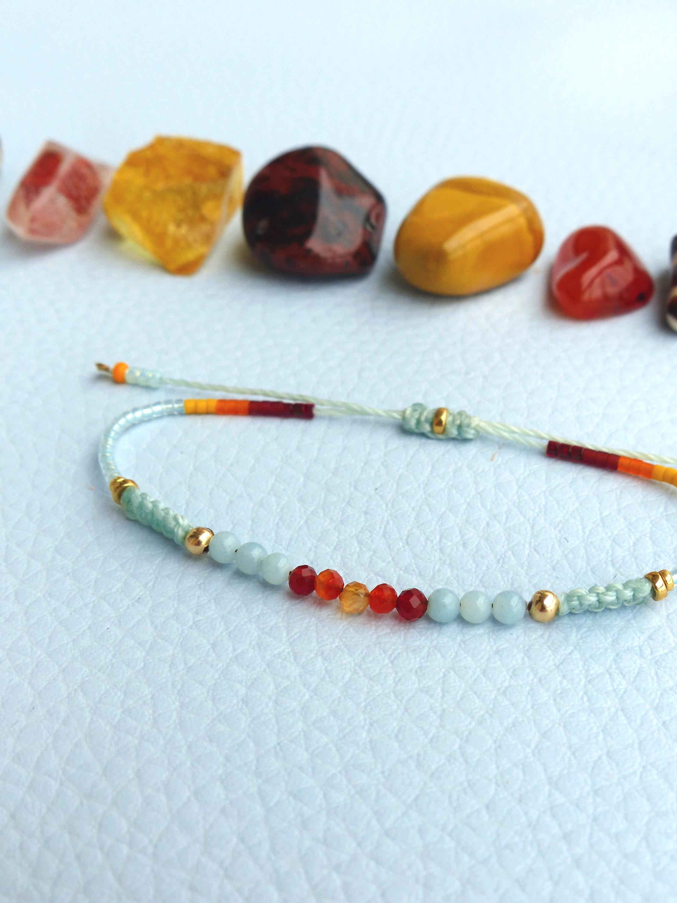 Peut inclure: Un bracelet délicat avec des perles bleu clair, des perles orange et rouges et des accents dorés. Le bracelet est fait avec un cordon fin bleu clair.