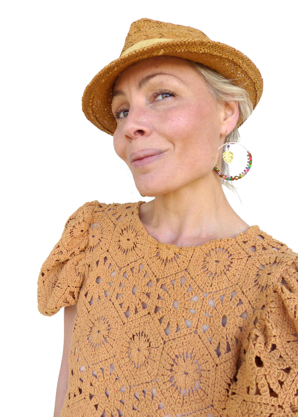 Peut inclure: Une femme portant un haut en crochet avec un chapeau de paille et des boucles d'oreilles créoles en perles colorées. Le haut est de couleur brun clair et présente un motif carré. Le chapeau est de couleur brun clair et a une large bordure. Les boucles d'oreilles sont faites de petites perles de différentes couleurs et ont un charme en feuille d'or.